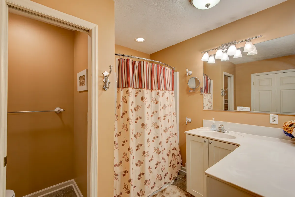 A calming bathroom with a floral-patterned shower curtain, generous vanity, and a large mirror under warm lighting. The space invites relaxation and supports the theme of rejuvenation and self-care.