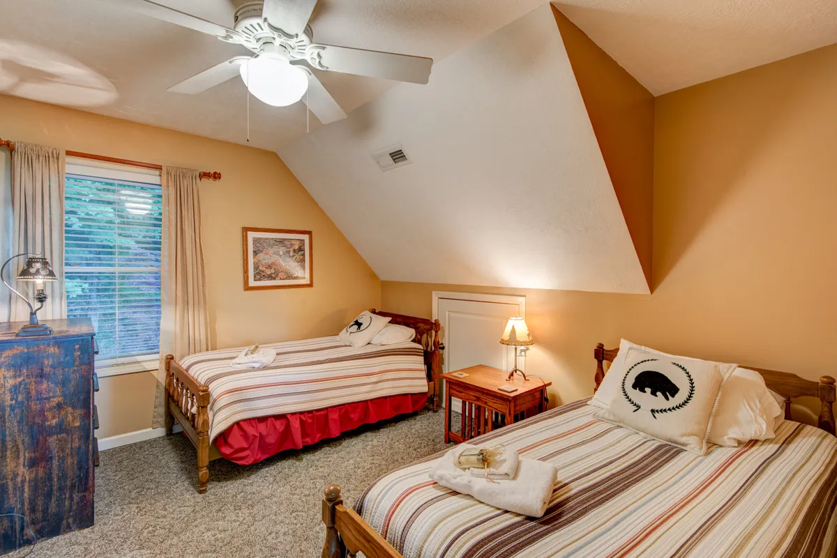 A bright and comfortable bedroom featuring two twin beds with striped bedding, a wooden dresser, and a window letting in natural light. The setup is ideal for siblings or friends and offers a sense of togetherness and fun.