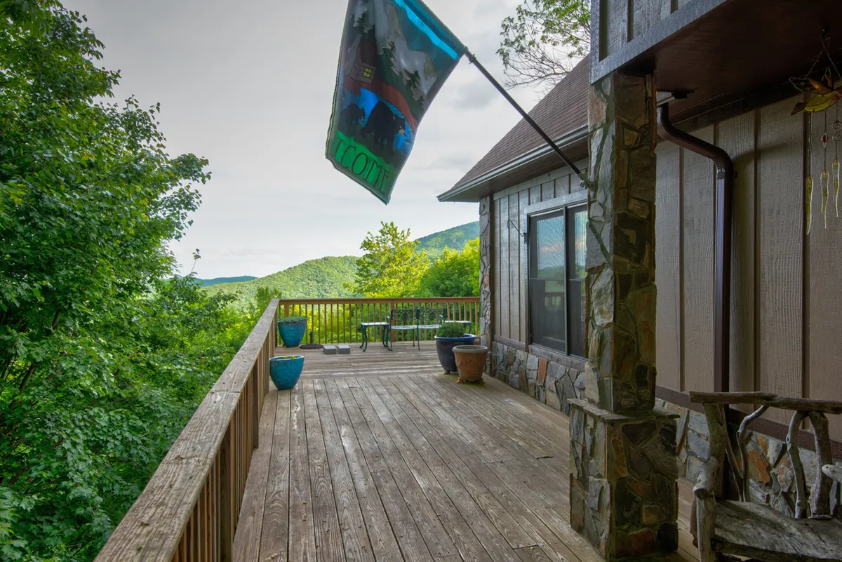 A deck with comfortable seating offers a direct view of the mountains, adorned with a flag fluttering in the breeze. The setting is ideal for relaxing, entertaining, or absorbing the peacefulness of nature, with the sun setting over distant peaks.