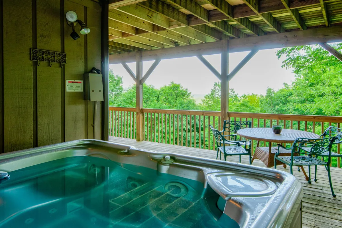 A tranquil outdoor setup with a bubbling hot tub and an adjacent dining table, surrounded by greenery. The area is inviting for both relaxation and socializing, ideal for unwinding after outdoor excursions or enjoying meals in the fresh air.