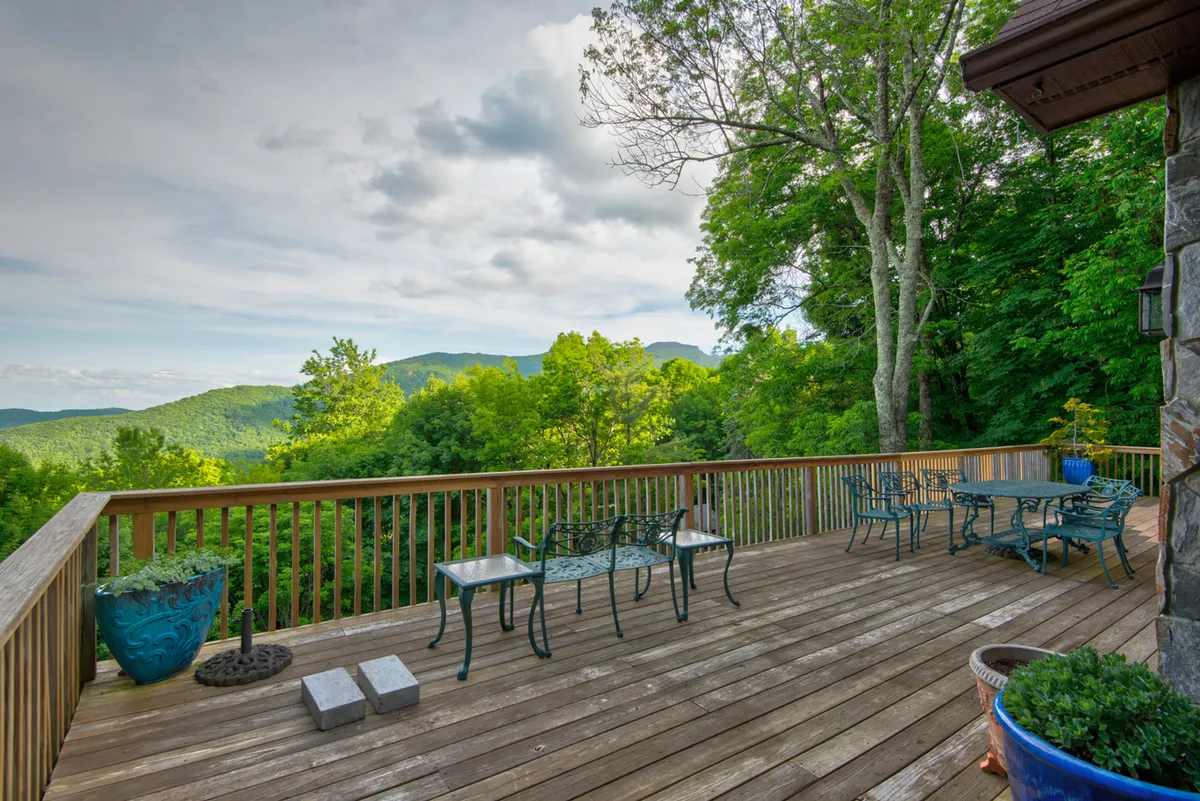 Deck seating faces an expansive view of rolling mountains, softened by planters and framed by trees. The tranquil mood invites guests to relax, enjoy morning coffee, or take in a brilliant sunset, surrounded by nature’s beauty.
