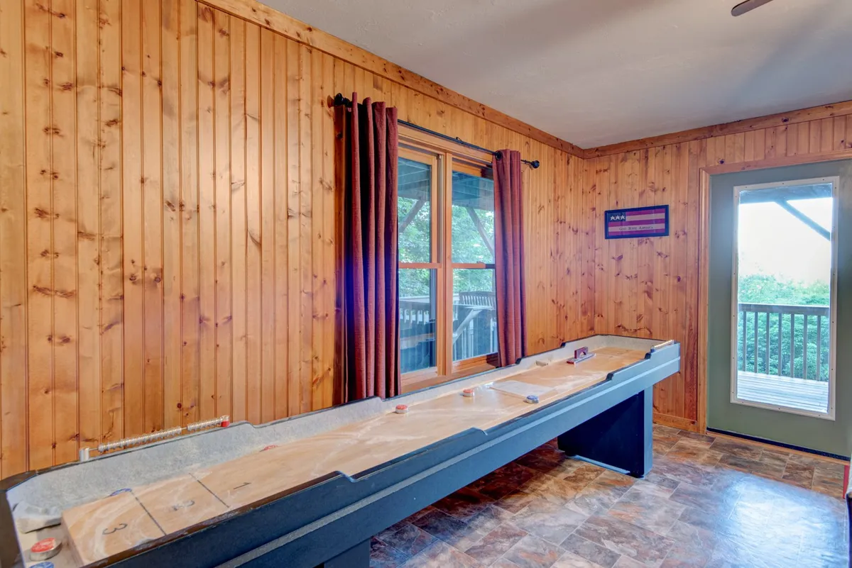 A shuffleboard table is the focus in this inviting interior, with large curtained windows allowing in soft natural light. The space feels playful and social, perfect for friendly games and family competitions, with ample room for movement and gathering.