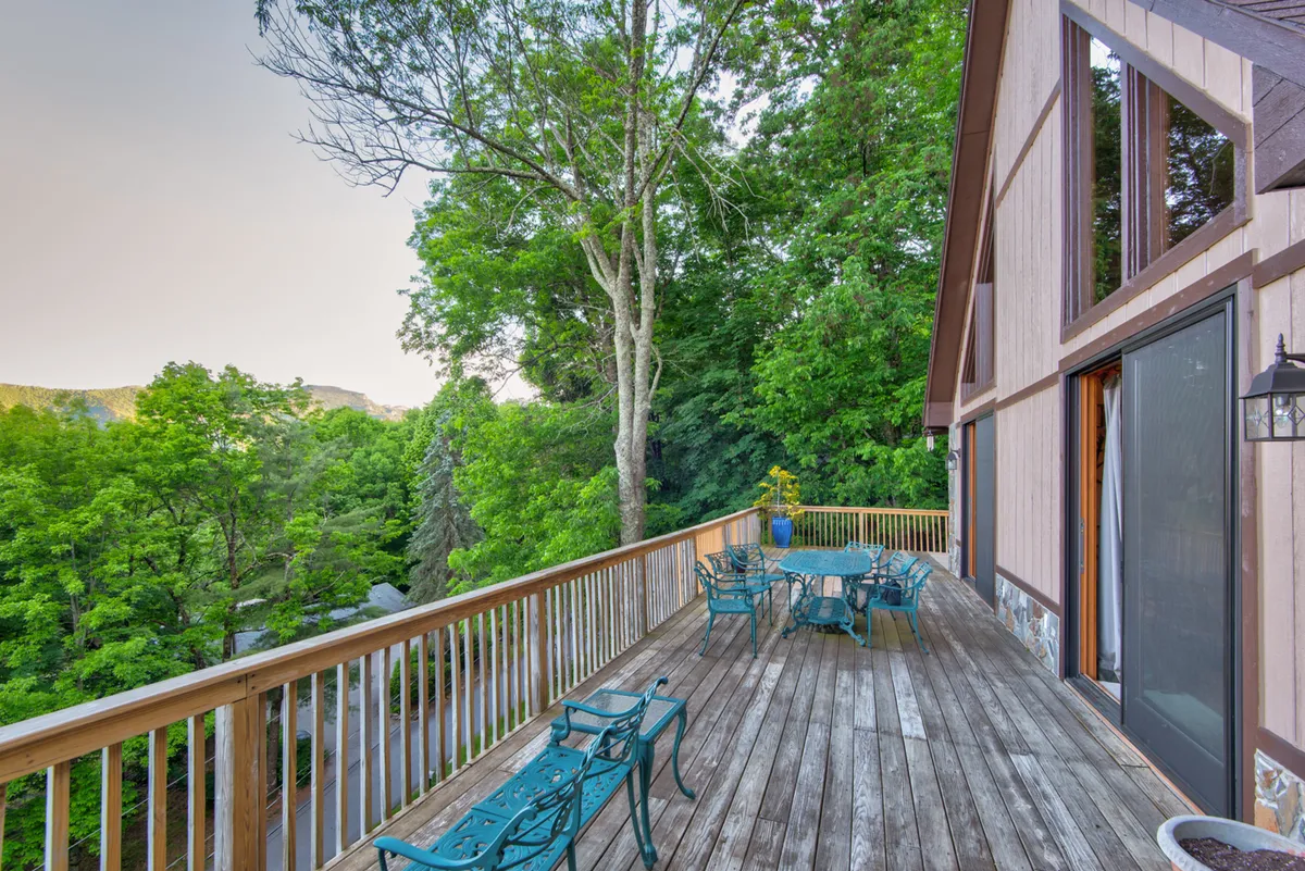 A spacious wraparound wooden deck furnished with metal patio furniture overlooks lush greenery and a stunning mountain vista. Designed for outdoor dining or morning coffee, the deck seamlessly extends the indoor gathering spaces into nature, inviting guests to soak in panoramic views at any time of day.