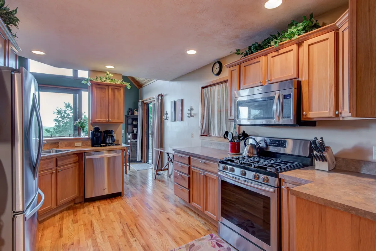A chef-grade kitchen gleams with stainless steel appliances and rich wooden cabinetry, a large kitchen island at its center perfect for meal prep and casual gatherings. Ample natural light streams in through generous windows, creating a warm, inviting backdrop for cooking and conversation.