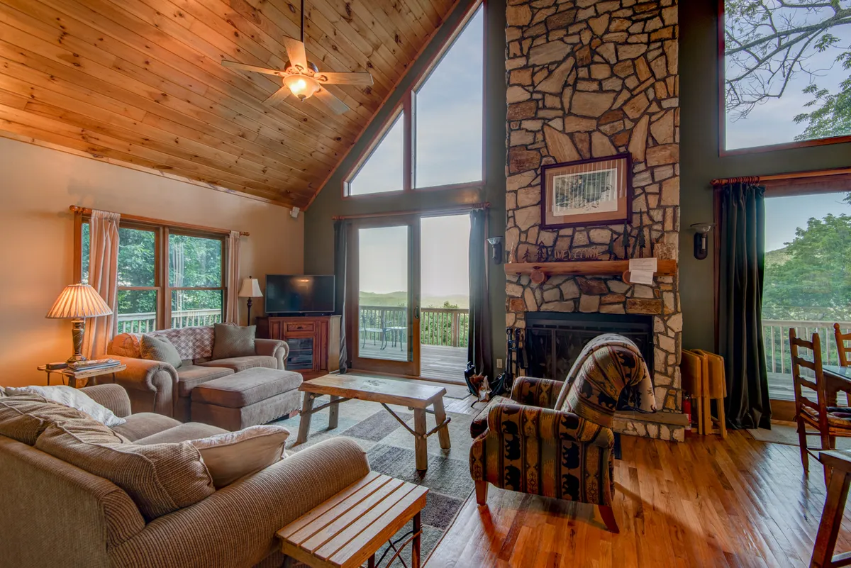 A warmly lit interior showcasing a large stone fireplace and tall windows that frame beautiful outdoor views. The inviting seating area promises a cozy retreat to unwind after outdoor exploits, with the fire offering comfort during crisp mountain evenings.